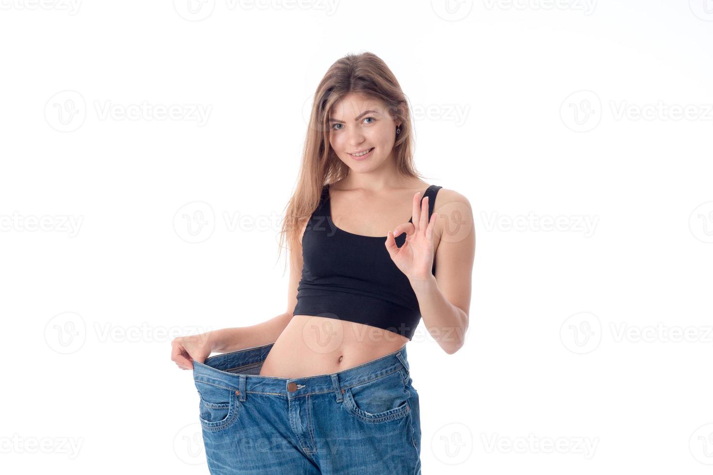 Slim girl stands in the big wide pants smiles and shows the hand gesture is isolated on a white background photo