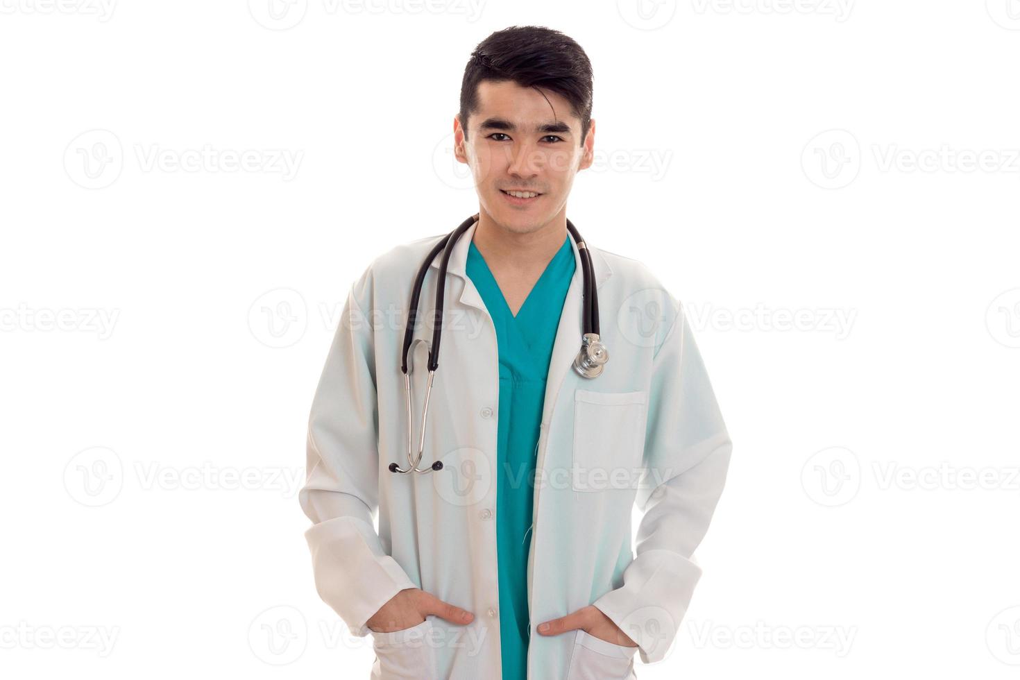 young handsome brunette man doctor in uniform with stethoscope on his shoulders looking and smiling on camera isolated on white background photo