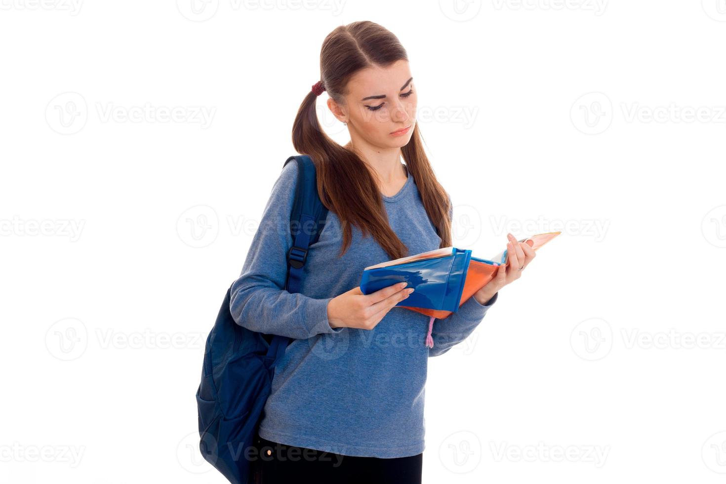 joven estudiante morena inteligente con mochila en los hombros lee un libro aislado de fondo blanco foto