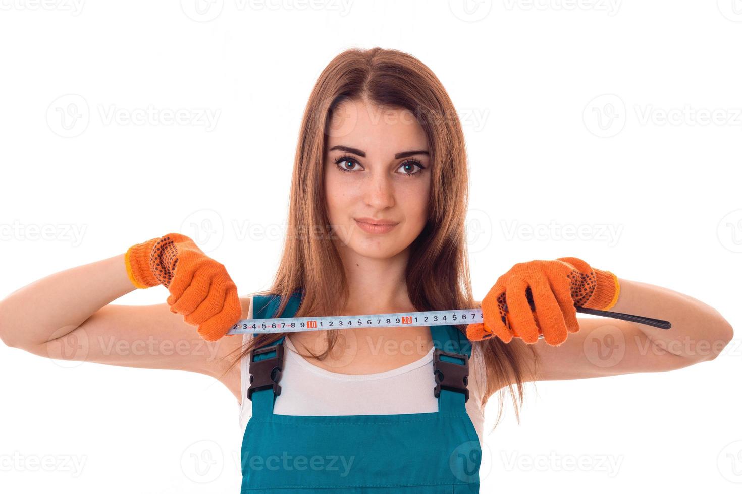 Una joven y encantadora morena constructora de uniforme con una herramienta de medida en sus manos hace renovaciones y mira la cámara aislada de fondo blanco foto