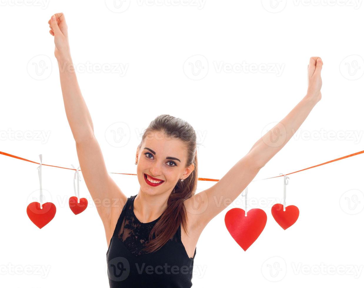 beautiful young girl in a black dress stands near the tape with cards in the form of hearts, smiles and raised her hands up photo