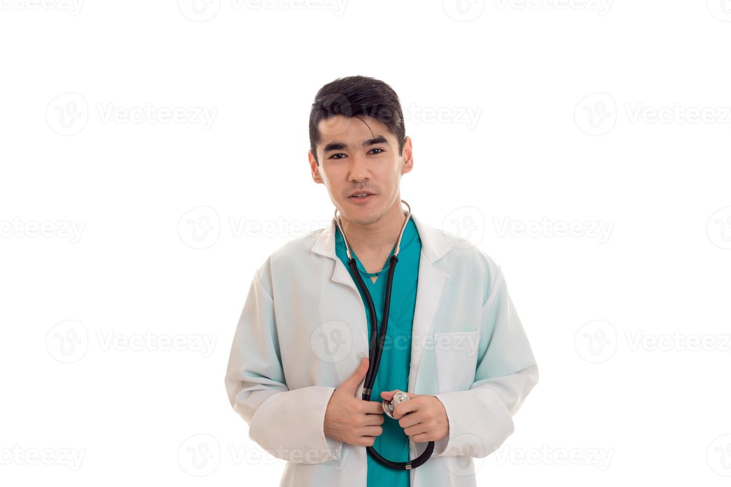 un joven médico con estetoscopio en túnica blanca mira la cámara foto