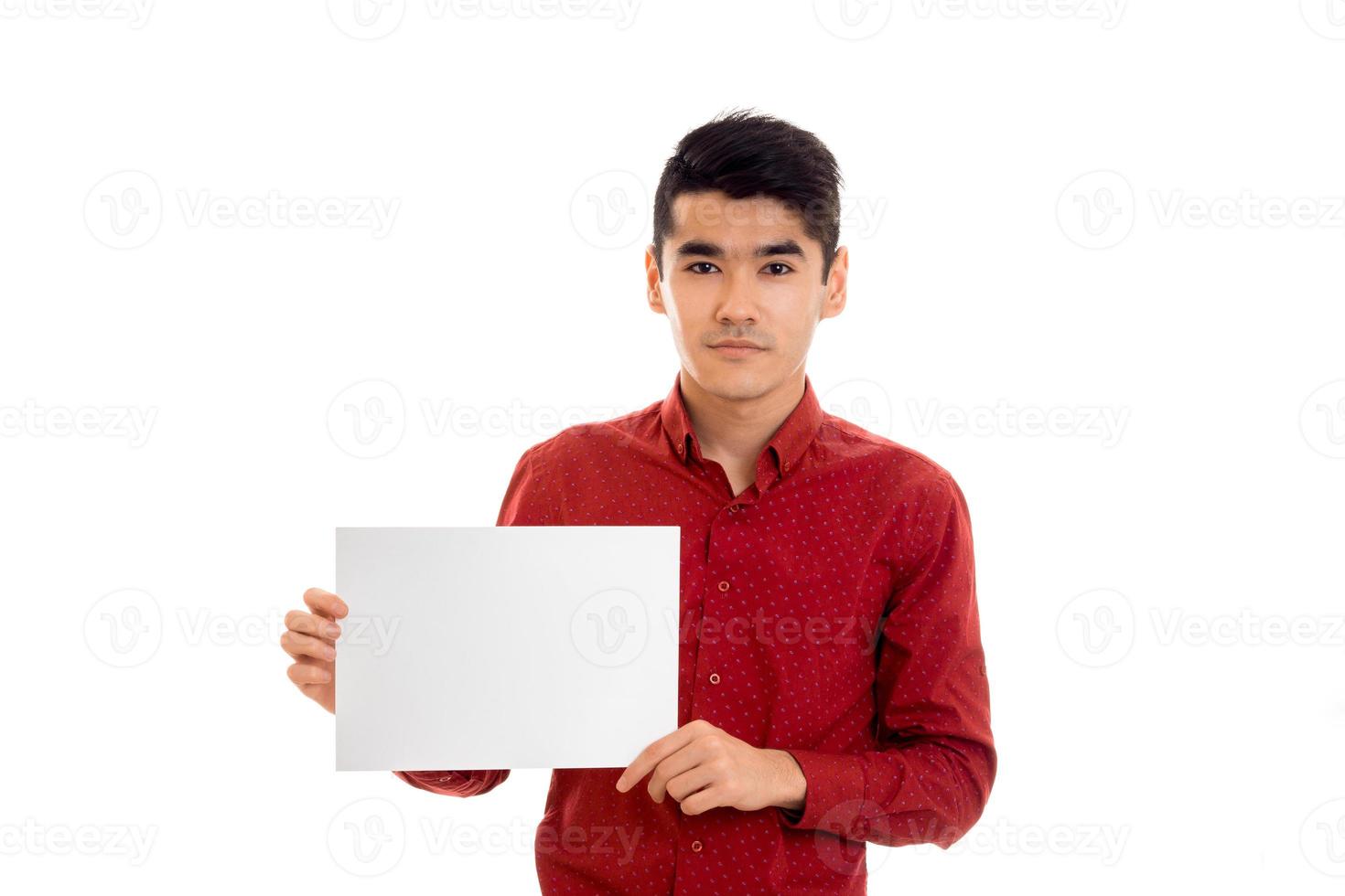 a young guy in a red shirt holding a white sheet of paper and looks into the camera photo