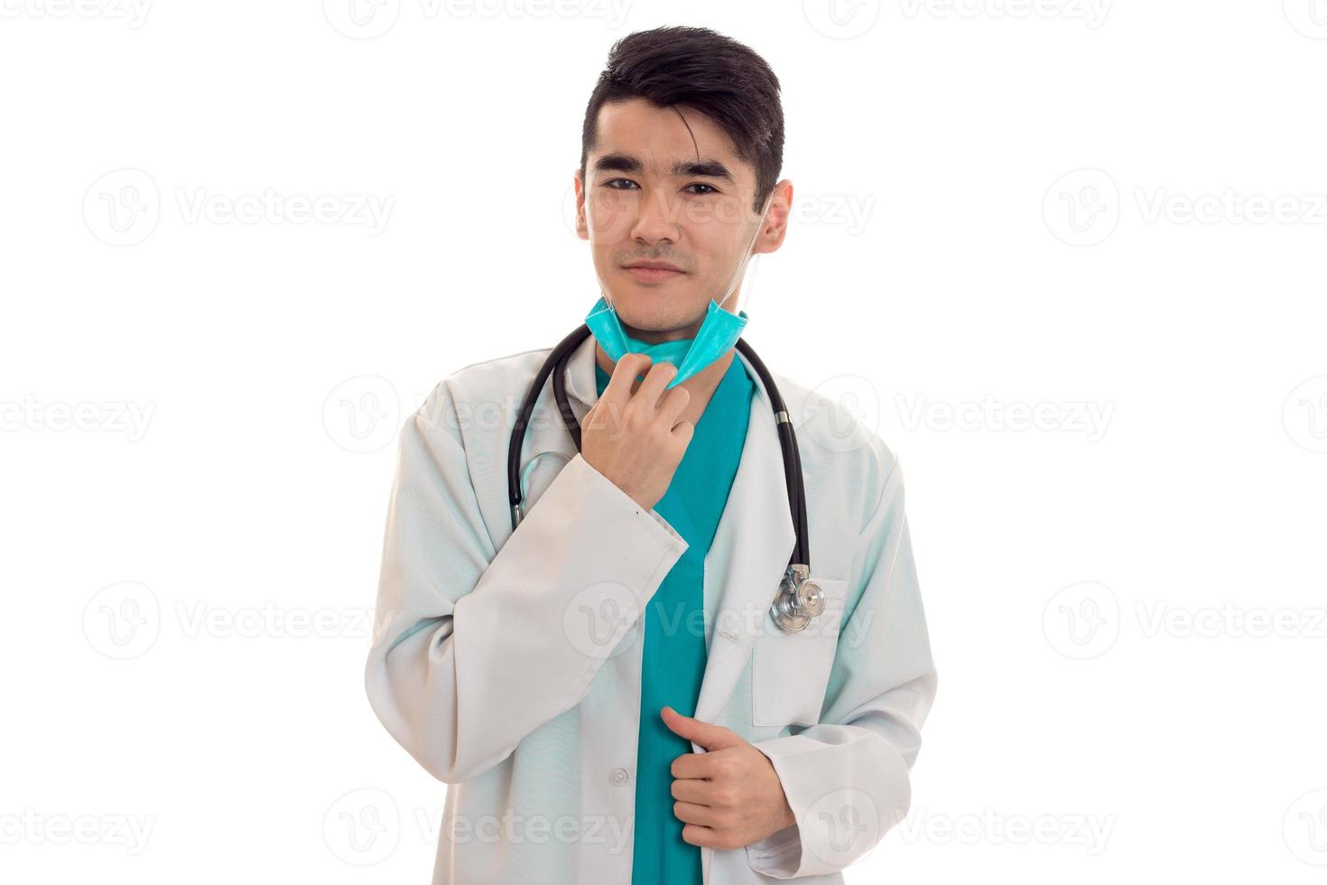 portrait of cute young brunette male doctor in uniform with stethoscope posing isolated on white background photo