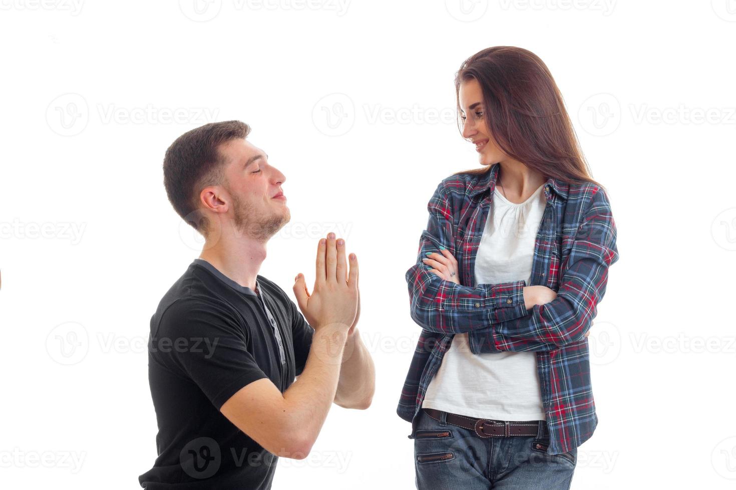 young guy kneels in front of the girl and asks for forgiveness and she is smiling photo