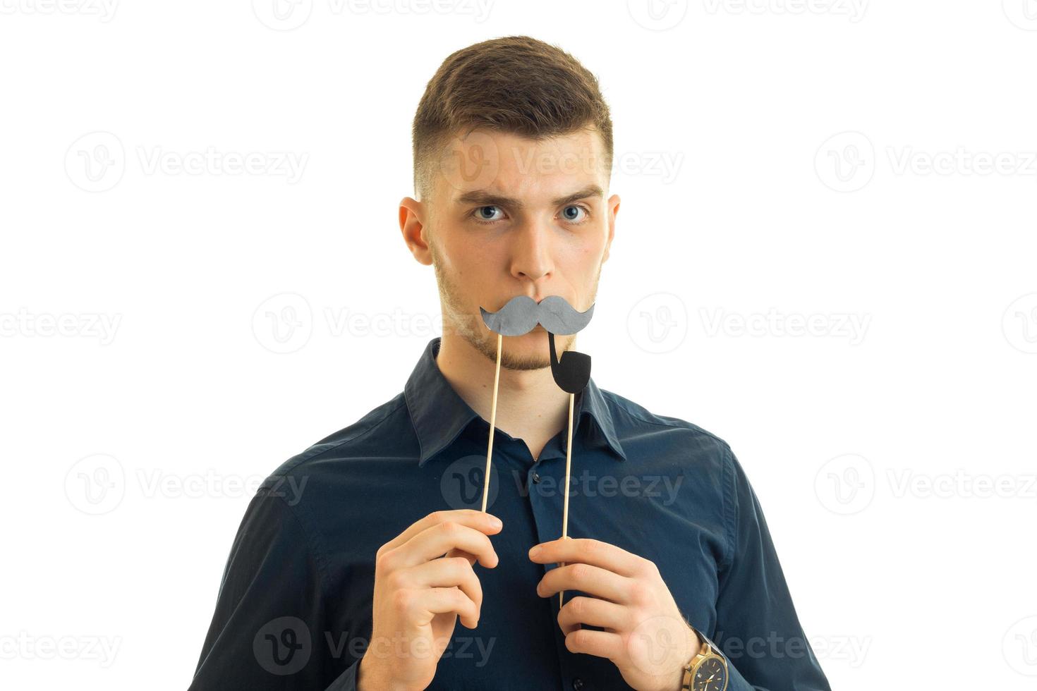 young charming guy keeps near the mouth paper mustache and looks into a camera photo