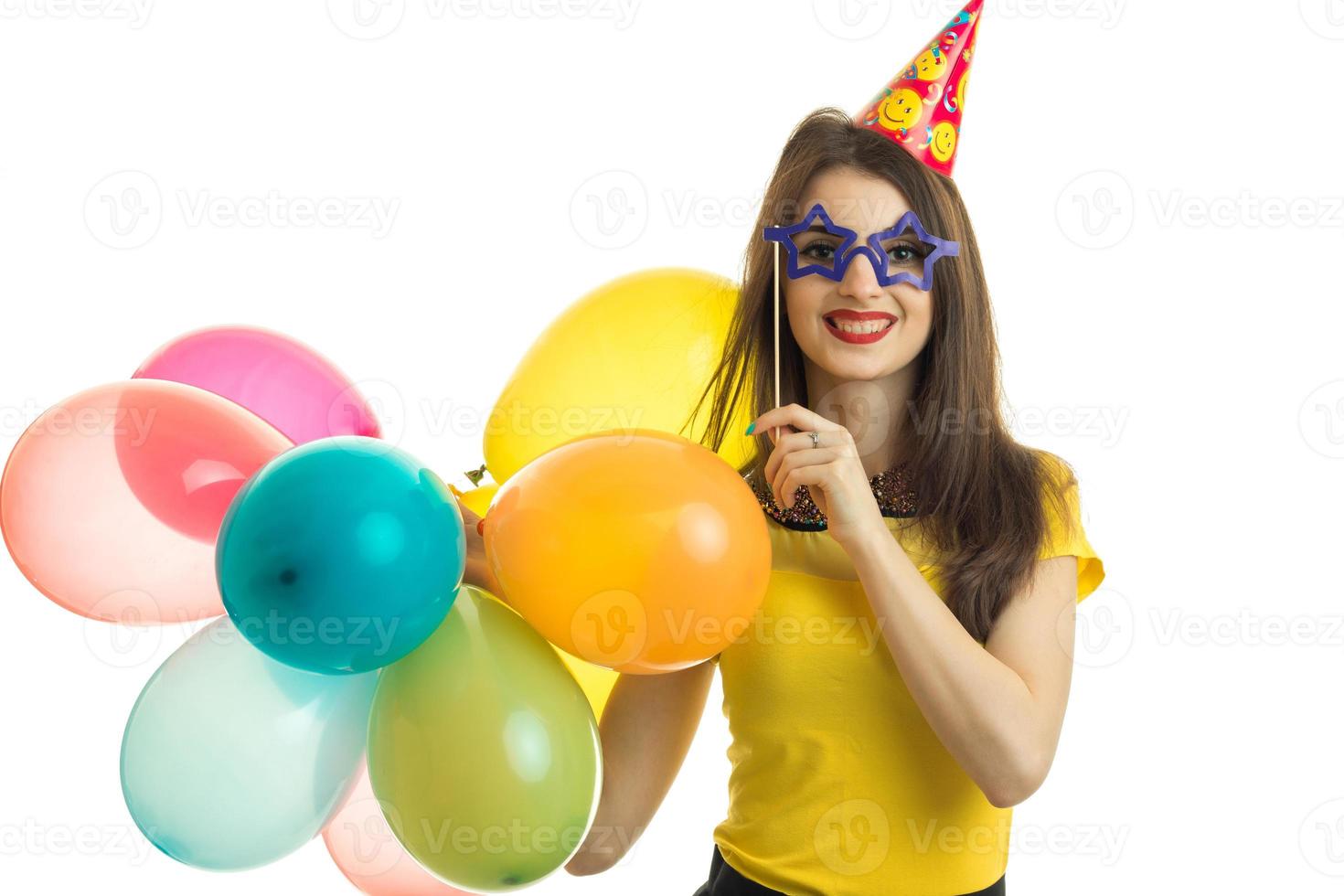 a cheerful young girl in a yellow blouse holding a big colored balls and artificial eye glasses photo