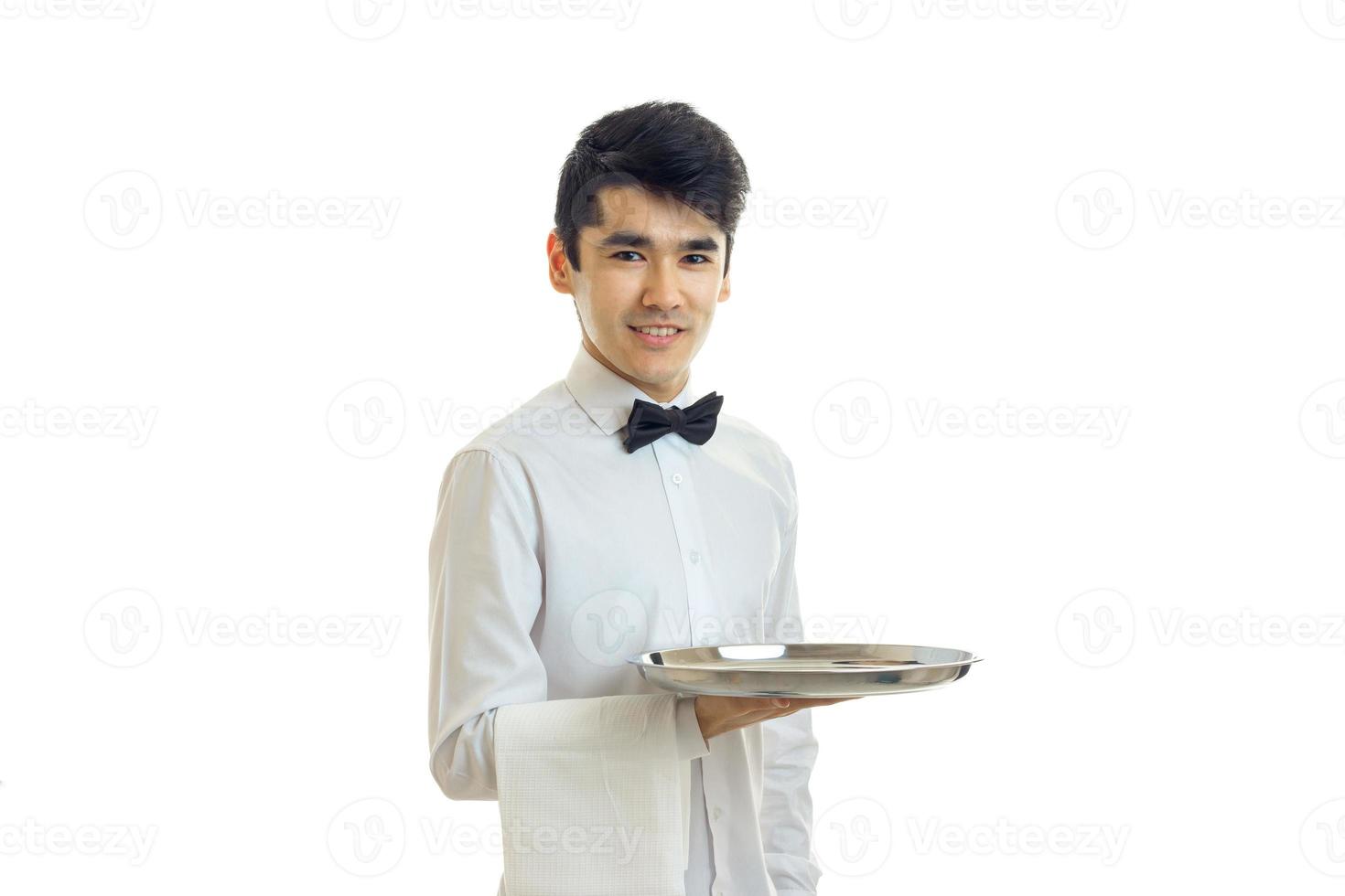 un joven camarero de cabello negro con una camisa blanca sonriendo y sosteniendo una bandeja foto