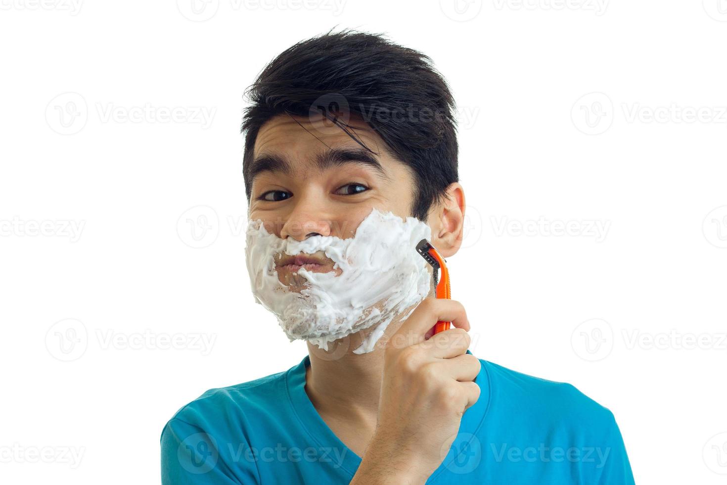 Portrait of a cheerful young man with foam on his face who shaves his beard machine close-up photo