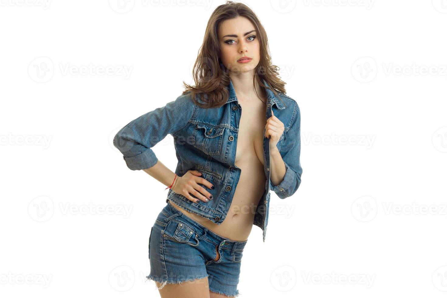 young beautiful brunette stands in jeans jacket keeps her hand on the side and looks toward photo
