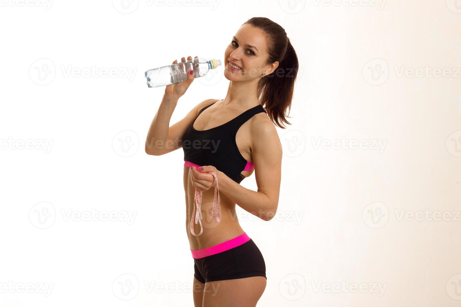 smiling sports girl stands sideways and drinks water from a bottle photo