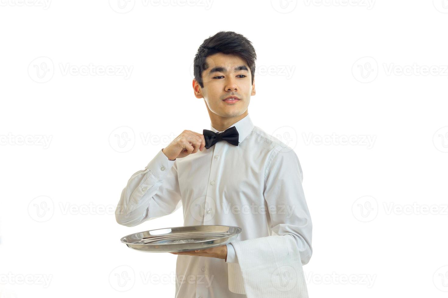 joven y apuesto camarero sosteniendo una bandeja y ajustando su arco foto