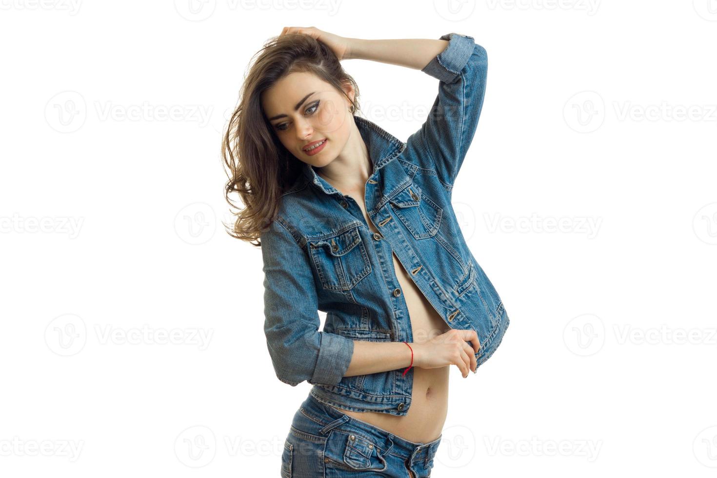 beautiful young girl with dark hair stands in jeans jacket and looks down photo