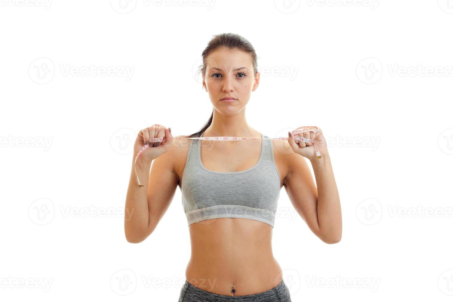 young beautiful slender girl in a gray top keeps itself the measuring tape in hand with serious face close-up photo