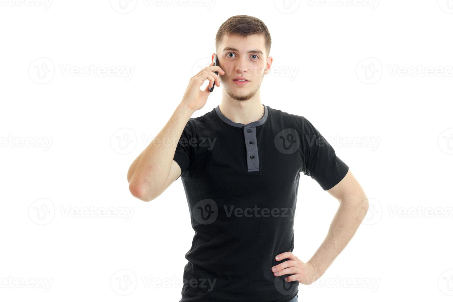 a charming young man in a black t-shirt looks straight and keeps a mobile phone near your ear photo
