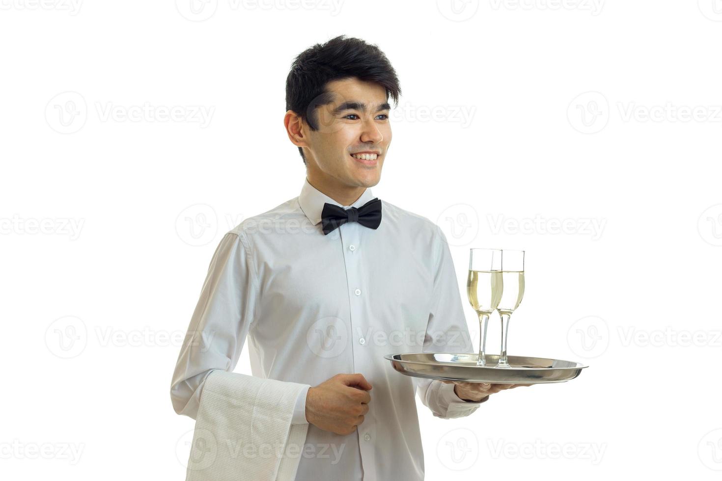 camarero guapo sonriente con cabello negro y camisa sosteniendo una bandeja con dos copas de vino foto