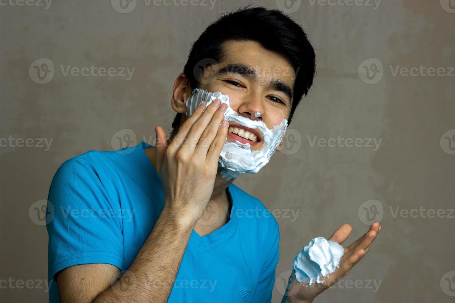 beautiful smiling guy with black hair is causing the foam to beard close-up photo