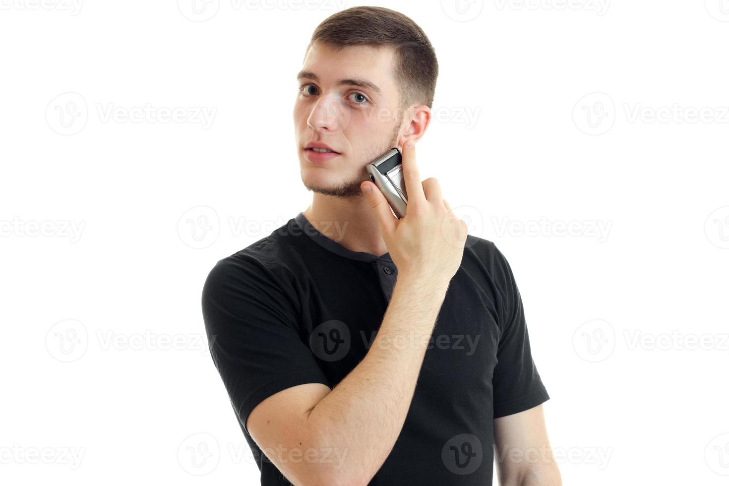 attractive young man in black t-shirt looks away and shaves a beard trimmer close-up photo