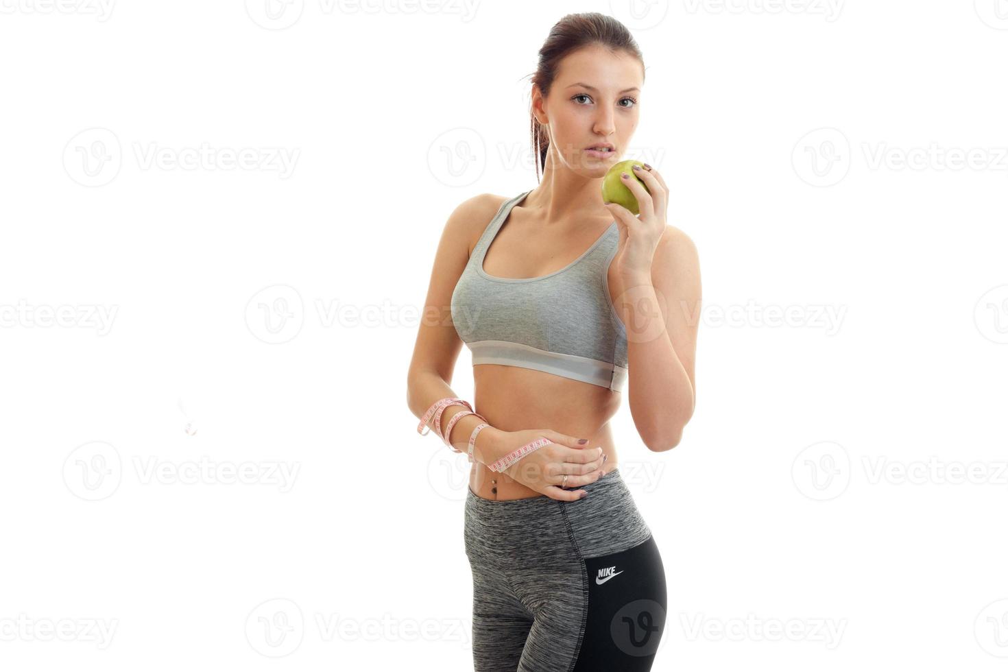 great athletic girl stands in fitness suit and eats Green Apple photo