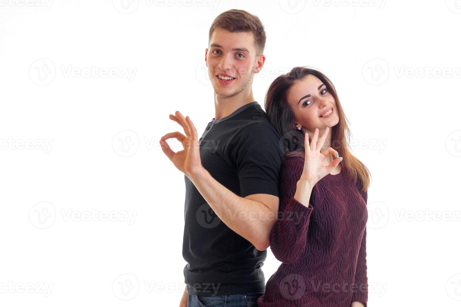 beautiful girl and a guy are standing back to each other smiling stare into the camera and show hands gestures photo