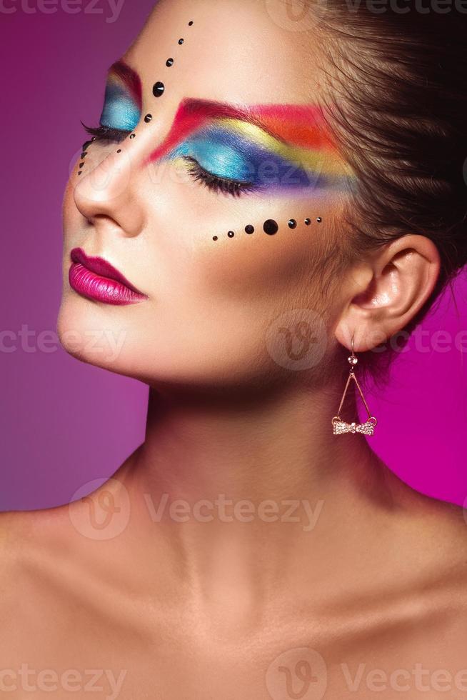 Vertical portrait of cute adult girl with multicolor make up on purple background photo