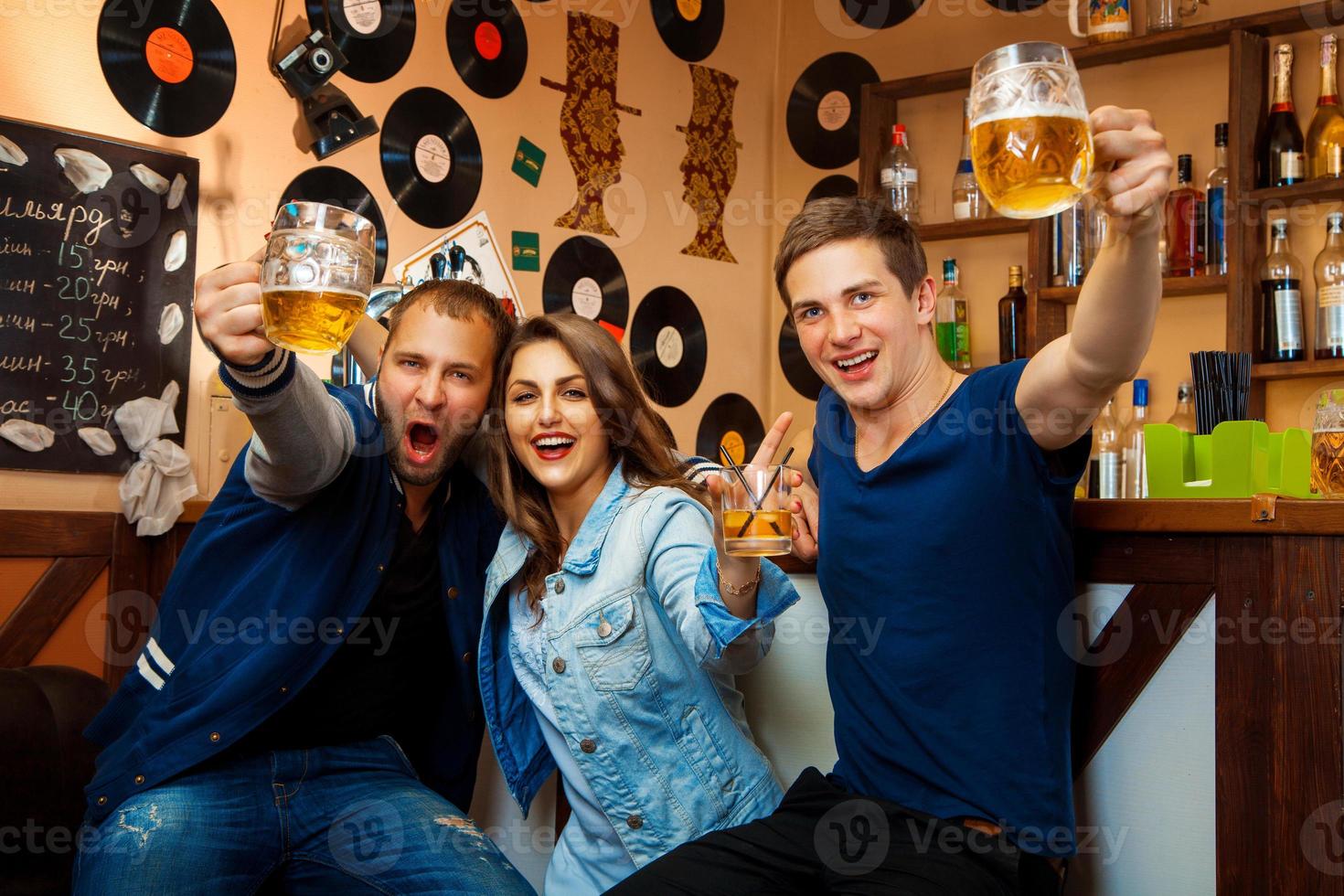fun company of two boys and one girl drink in bar photo