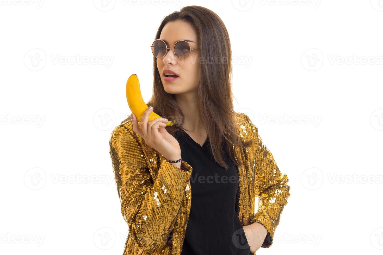 beautiful glamour girl in round spectacles in the gold jacket keeps the banana in hand photo