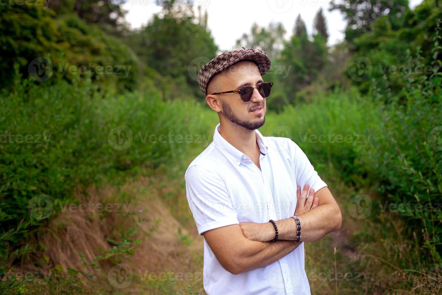 Glamour young man model in hat holds sunglasses and looking away outdoors photo