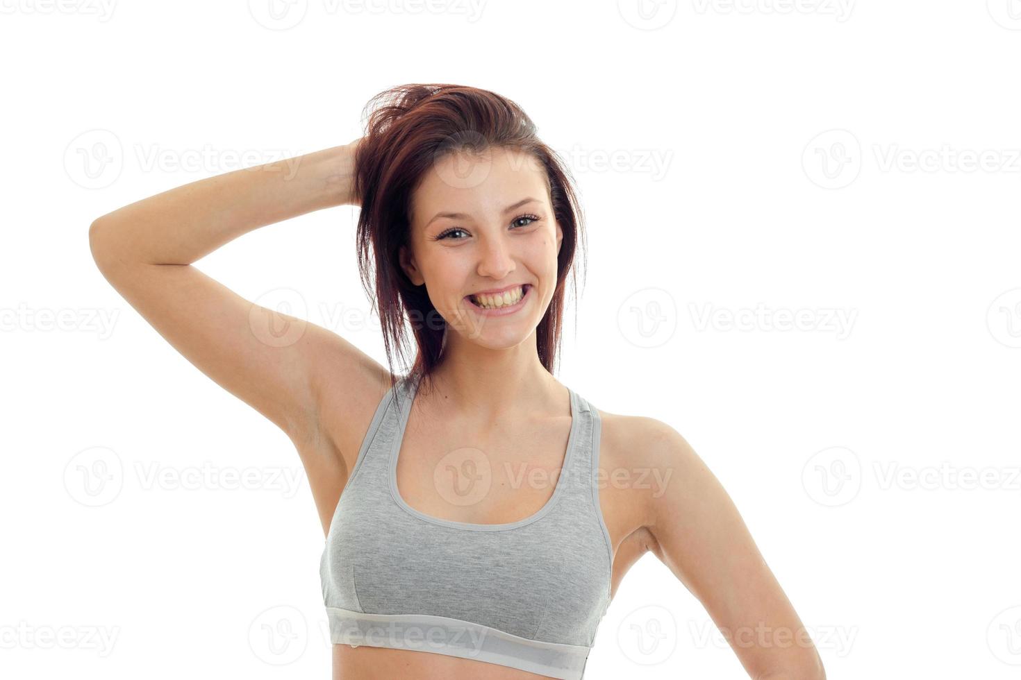 horizontal portrait of joyous beautiful brunette that stands in a gray top looks straight and laughs photo