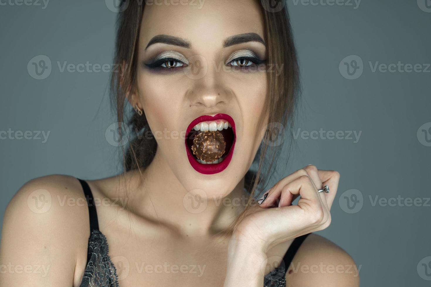 young girl with red lips eats chocolate candy and looking at the camera photo