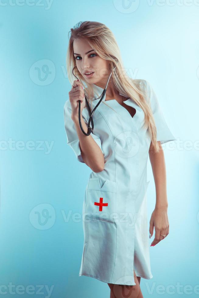 Sweet blonde nurse with stethoscope in white medical gown photo