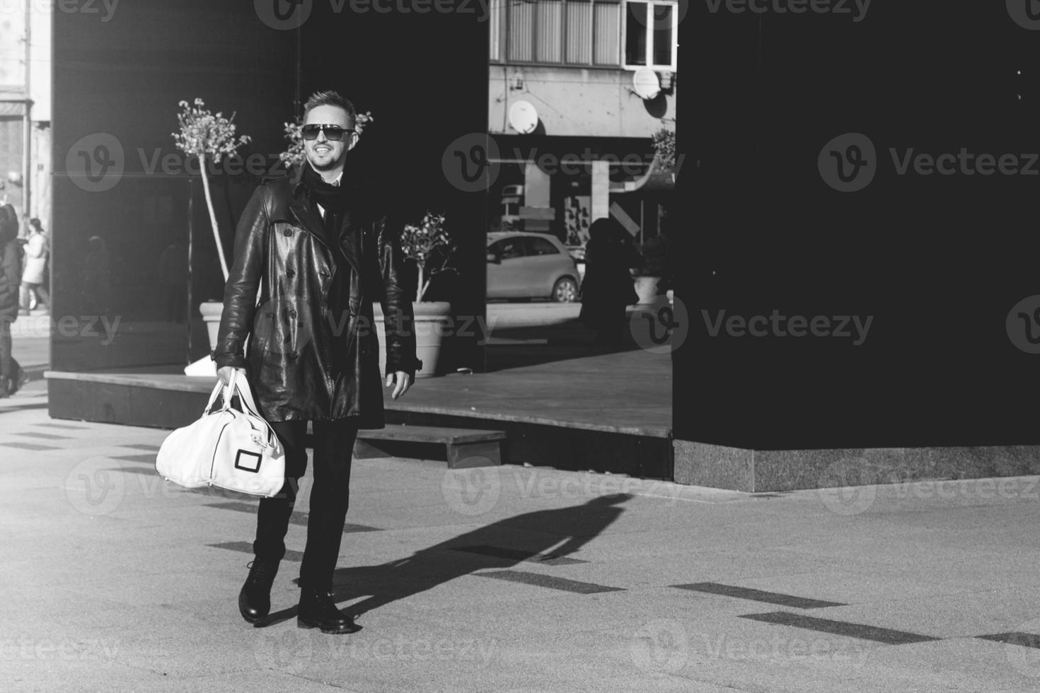 Black and white photo of beauy male model in sunglasses walking down the street