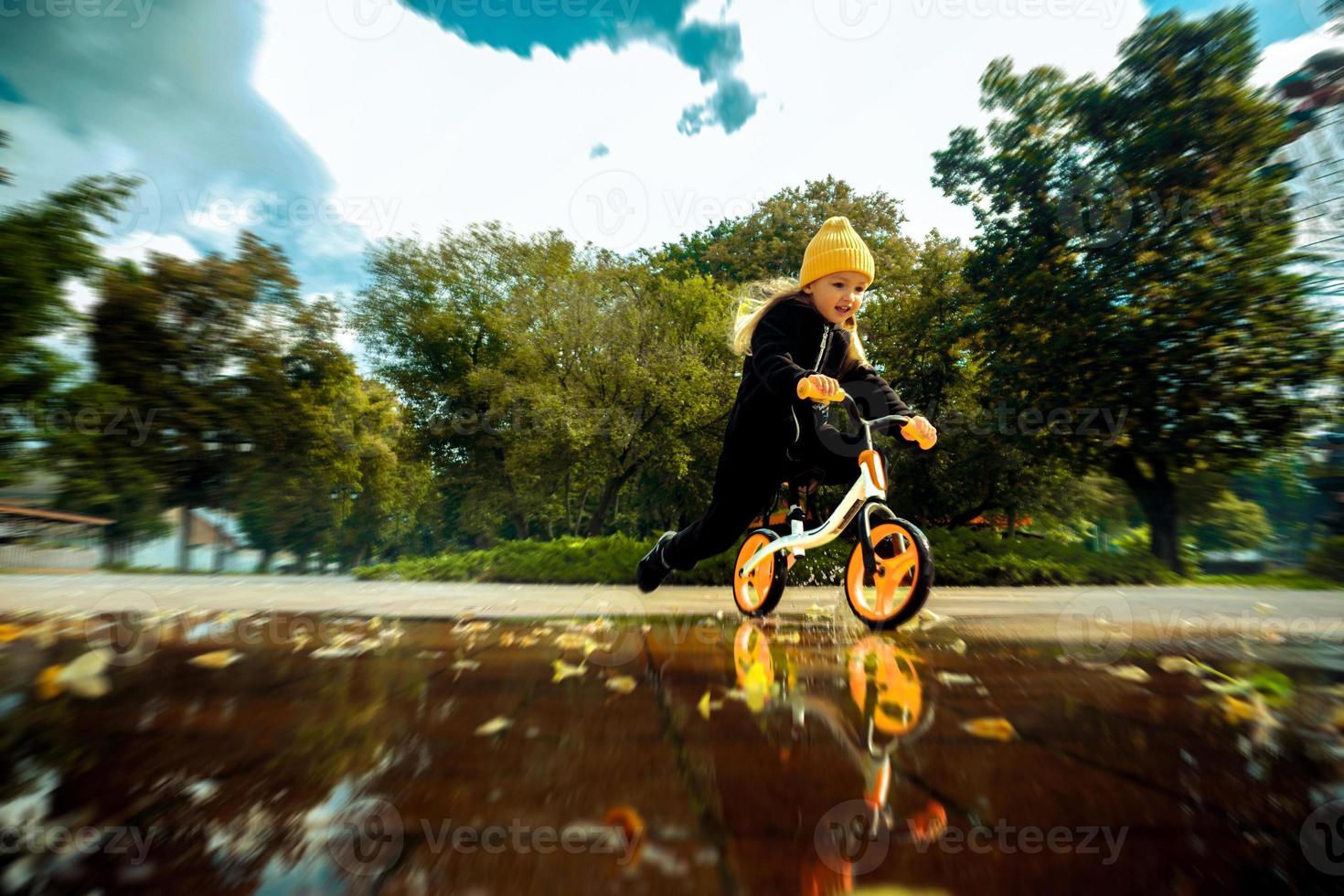 Cutie little girl rides through the puddles on bicycle at the park photo
