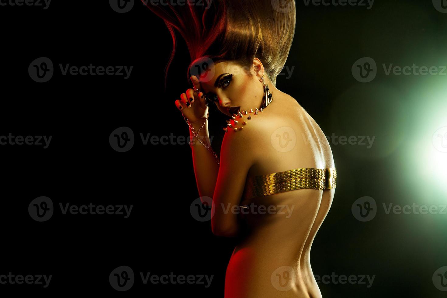 Charming young sexual woman with high creative hairstyle and golden accessories in studio photo