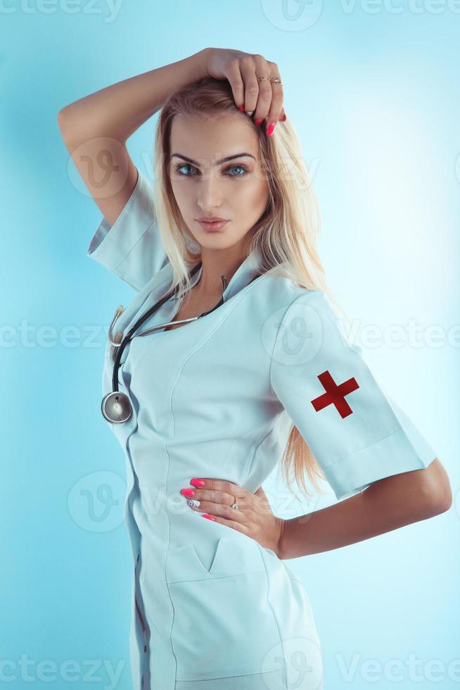 Enfermera rubia atractiva en bata médica blanca con estetoscopio foto