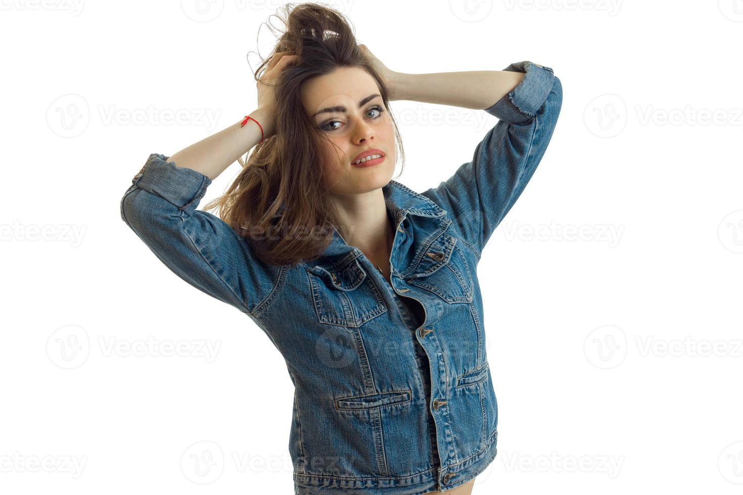 beautiful smiling girl standing in jeans jacket and keeps hands hair photo