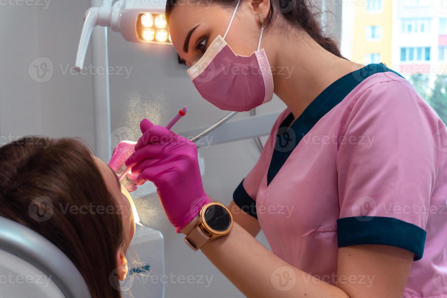 dentist in pink uniform treat the teeth of a patient photo