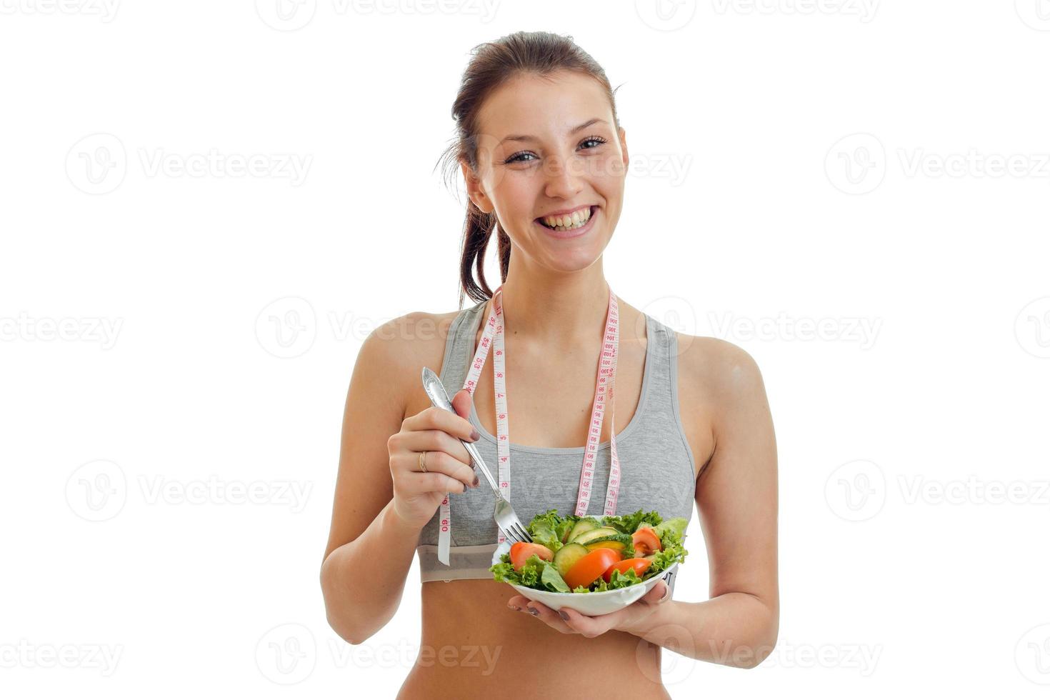 hermosa chica feliz mirando a la cámara, riendo y sosteniendo un plato con ensalada de verduras cerrada foto