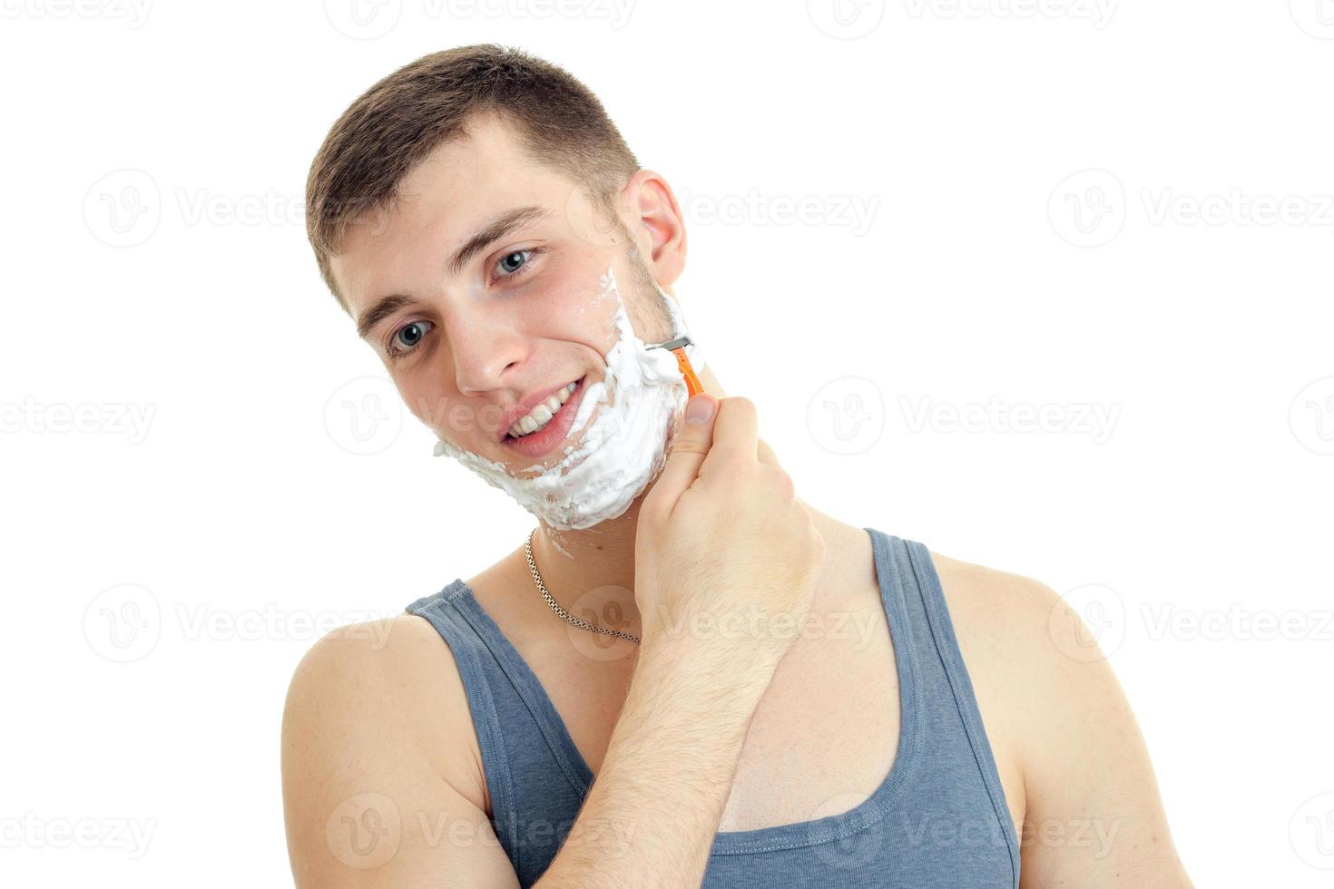 un joven alegre con espuma en la cara que vale la pena doblar la cabeza sonriendo y afeitándose la barba está aislado en un fondo blanco foto