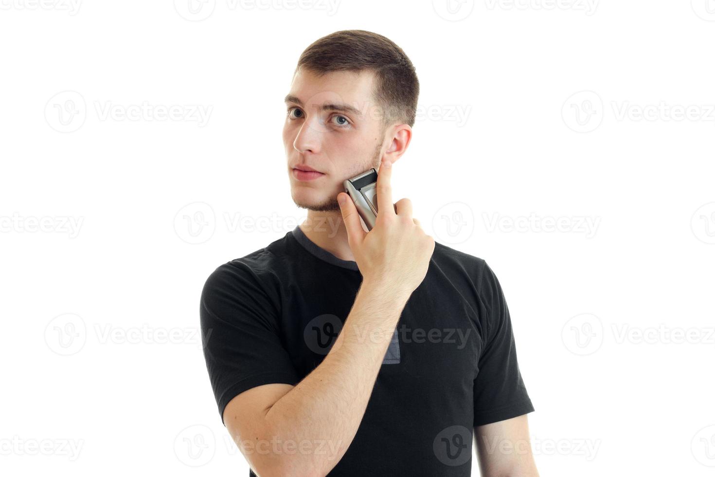 handsome young strong guy in a black t-shirt and looks toward shaves his beard close-up photo