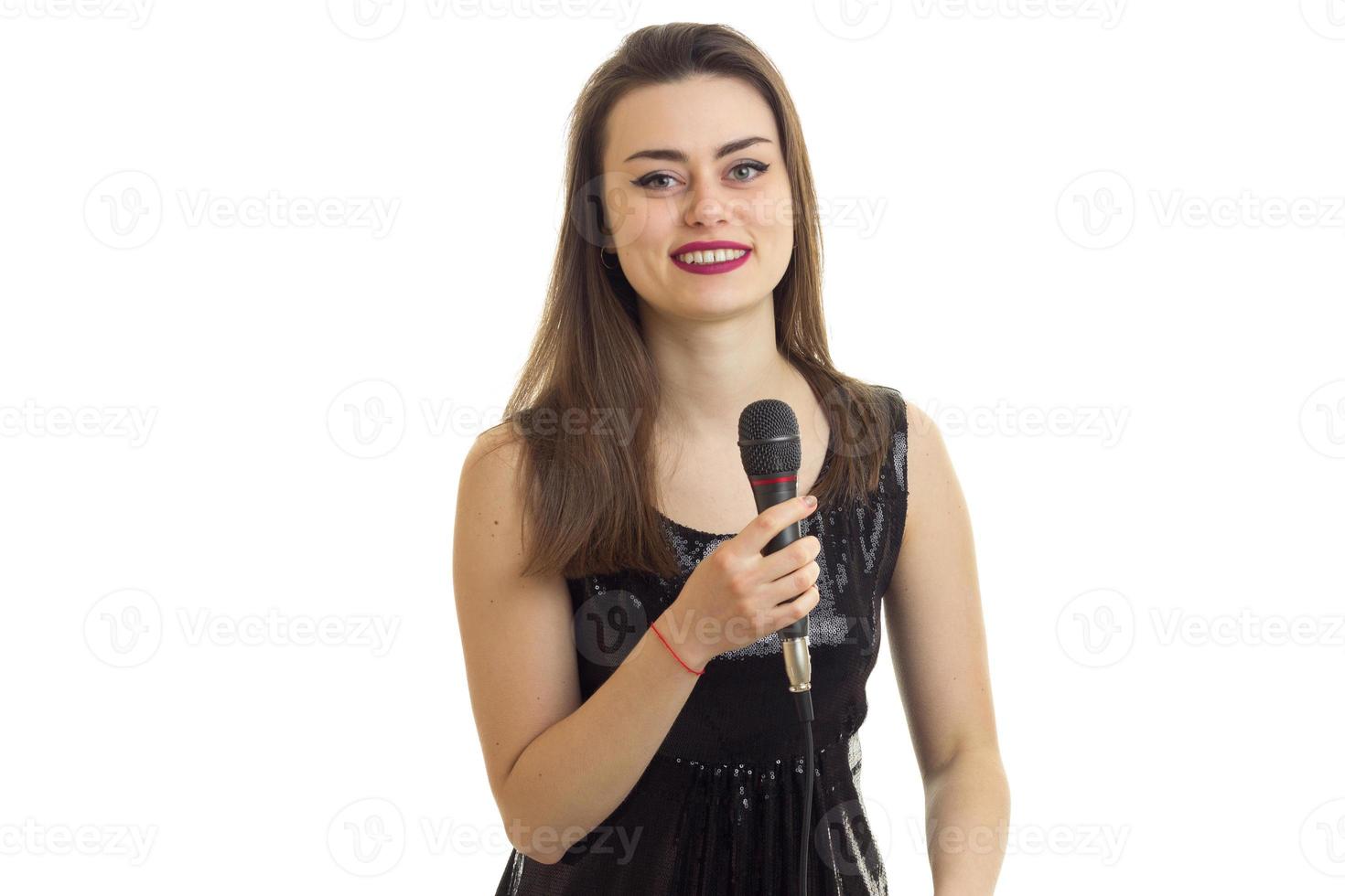 cheerful young woman in black dress smiles with microphone in hands photo