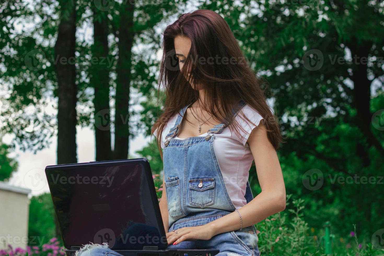 young cute brunette with long hair sitting in a park with a laptop photo