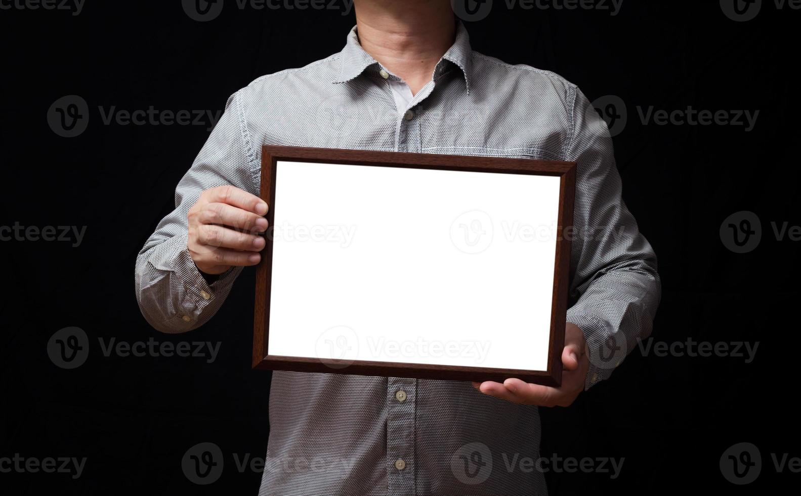 A blank diploma or a mockup certificate in the hand of a man employee wearing a shirt on black background. The horizontal picture frame is empty and the copy space. photo