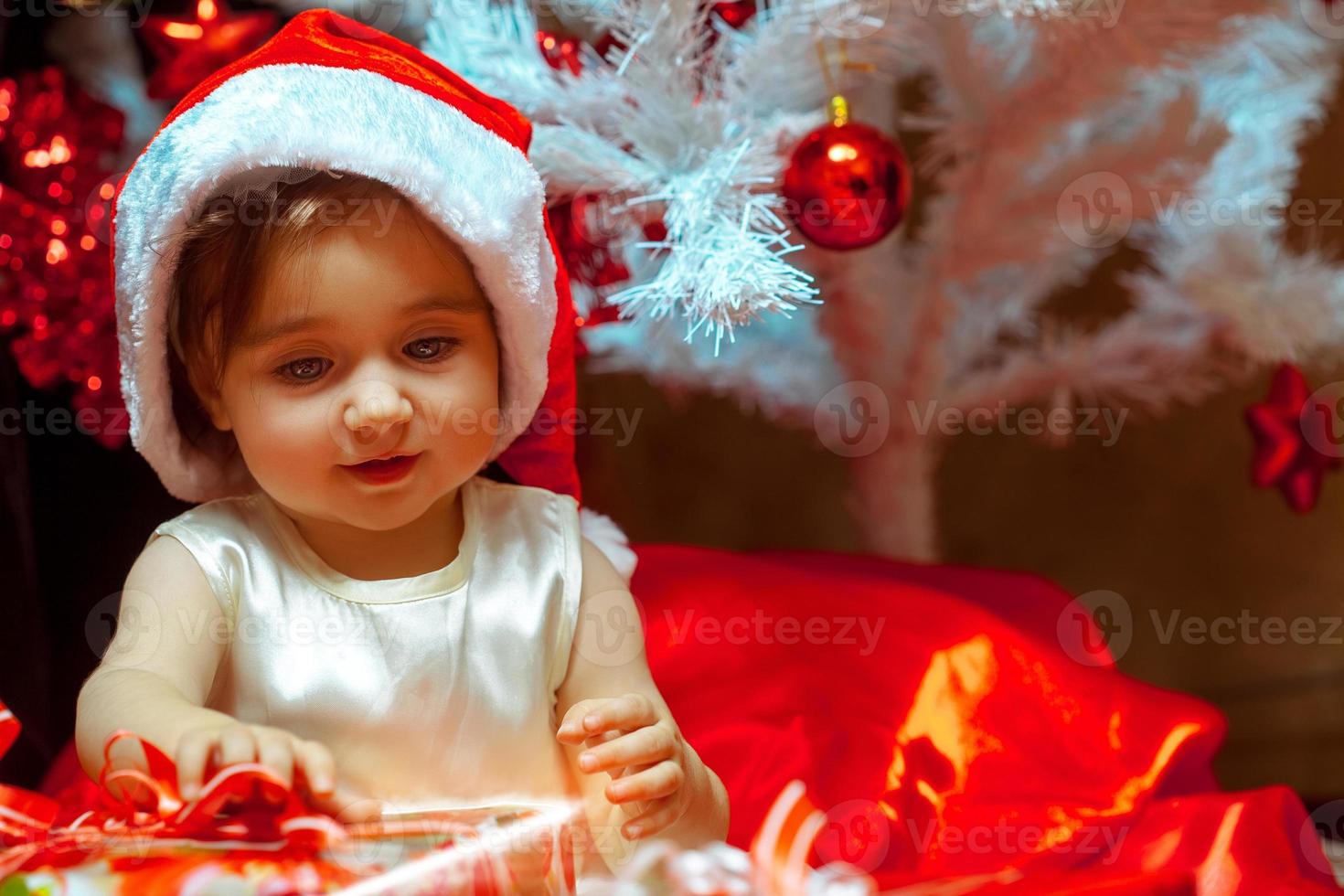 la niña desempaqueta el regalo debajo del árbol de navidad foto