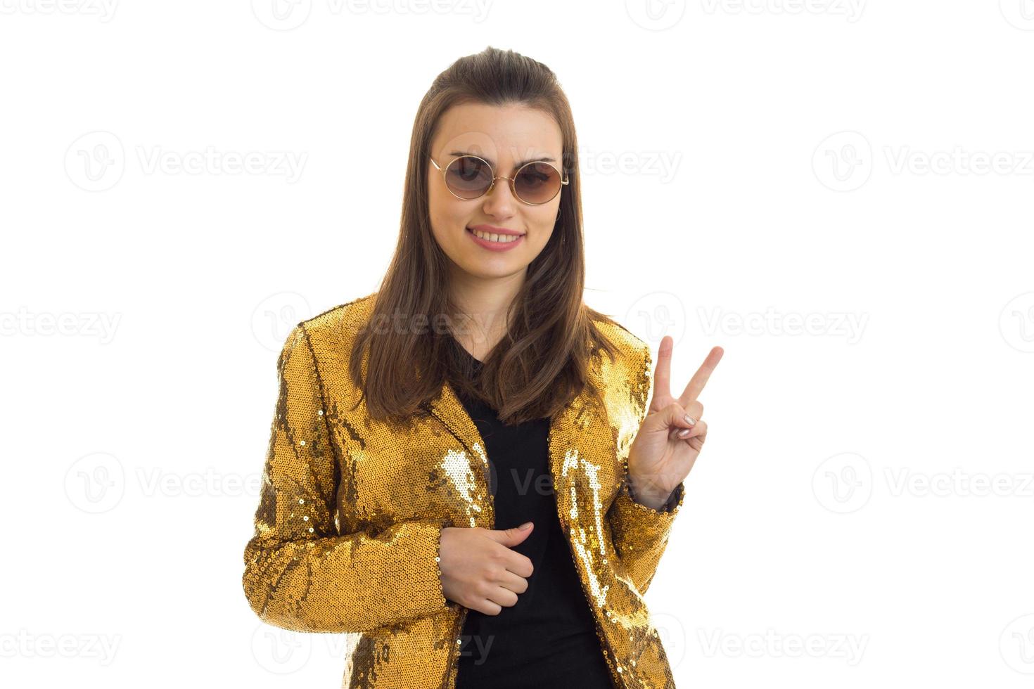 Cute woman in round sunglasses and golden jacket showing peace gesture photo