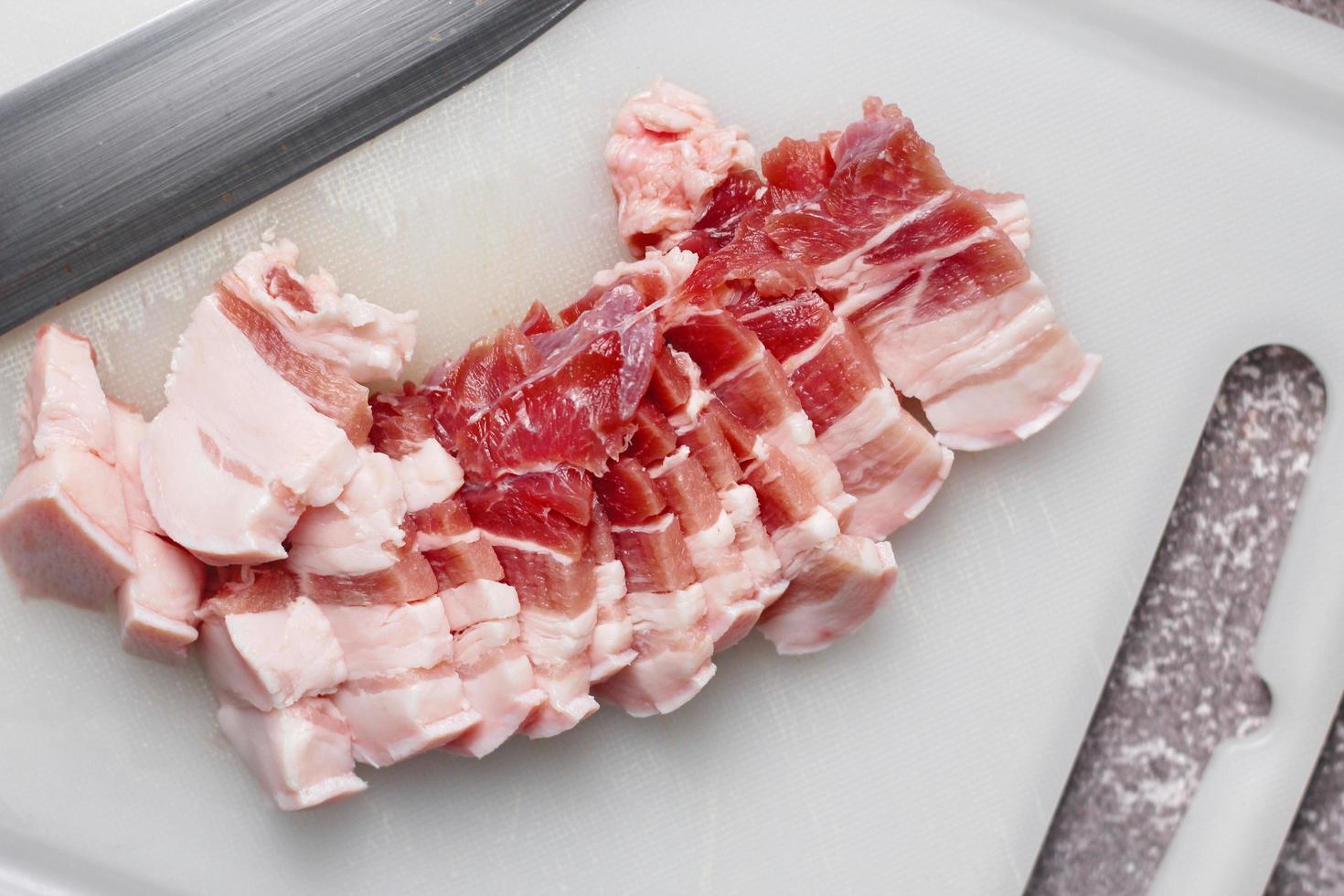 streaky pork is sliced on a white chopping board in the kitchen.Close up cutting slide pork belly raw photo