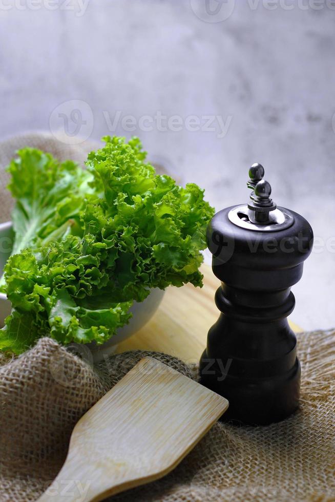 lechuga colocada en un tazón blanco y una tabla de cortar sobre una mesa blanca. ensalada de vegetales. comida vegetariana. comida limpia vegetales verdes. foto