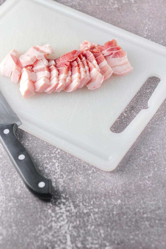 streaky pork is sliced on a white chopping board in the kitchen.Close up cutting slide pork belly raw photo