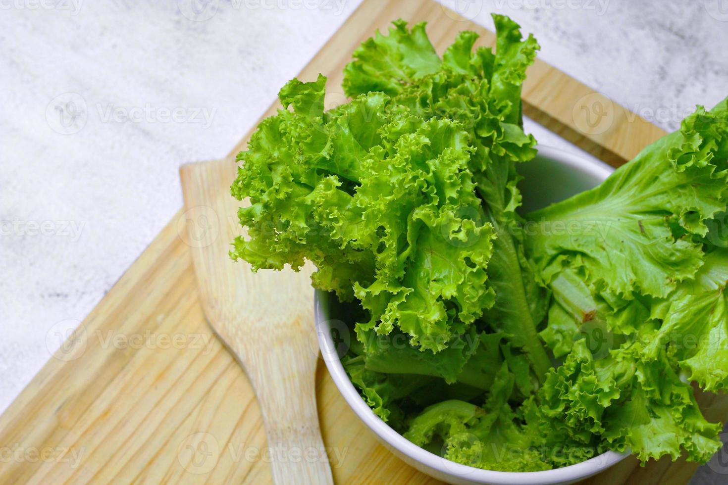 Lettuce placed in a white bowl and a cutting board on a white table. Vegetable salad. Vegetarian food. Clean food. Green vegetables. photo