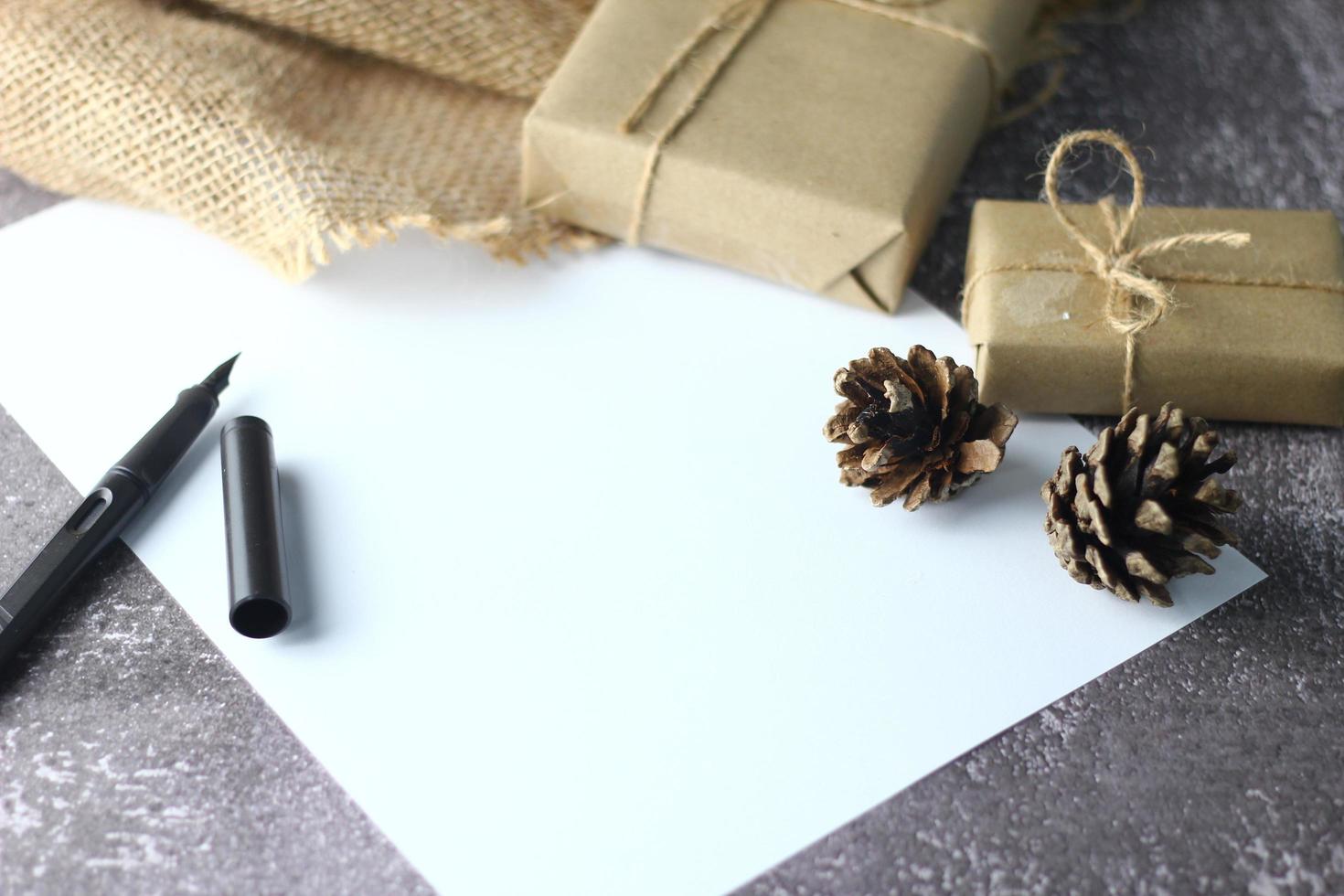 Holidays Gifts. Christmas and New Year.Gift box wrapped in brown paper pine cones and white paper and pens placed on the table, copy space. photo